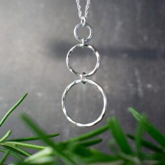 necklace featuring 3 circles of increasing size. Hung over black background with rosemary greenery