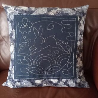 A navy and silver metallic fabric cushion with a hand embroidered rabbit panel in sashiko style