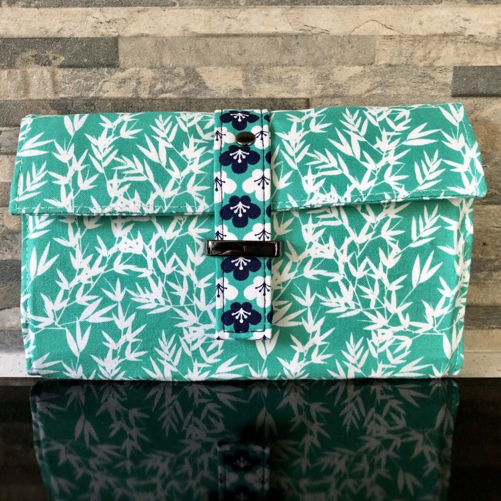 Handcrafted clutch wallet in green floral fabrics and gunmetal hardware. Closes with a simple flap strap.