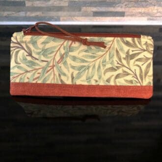 A zipped pencil case a green and brown Willow design by William Morris with faux suede pull, pale pink lining on shiny black surface.
