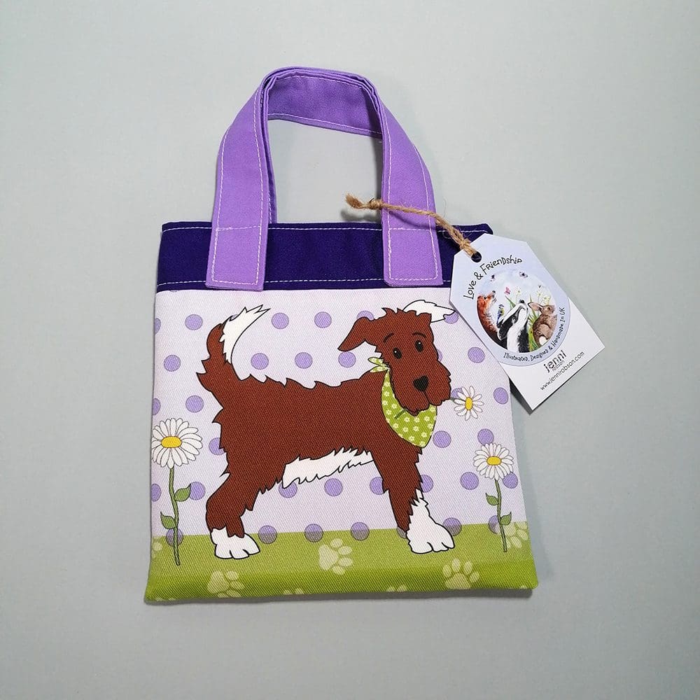 Front view of the mini bookbag in two shades of purple cotton fabric adorned by a brown dog in a green bandana. Lined with water resistant lining