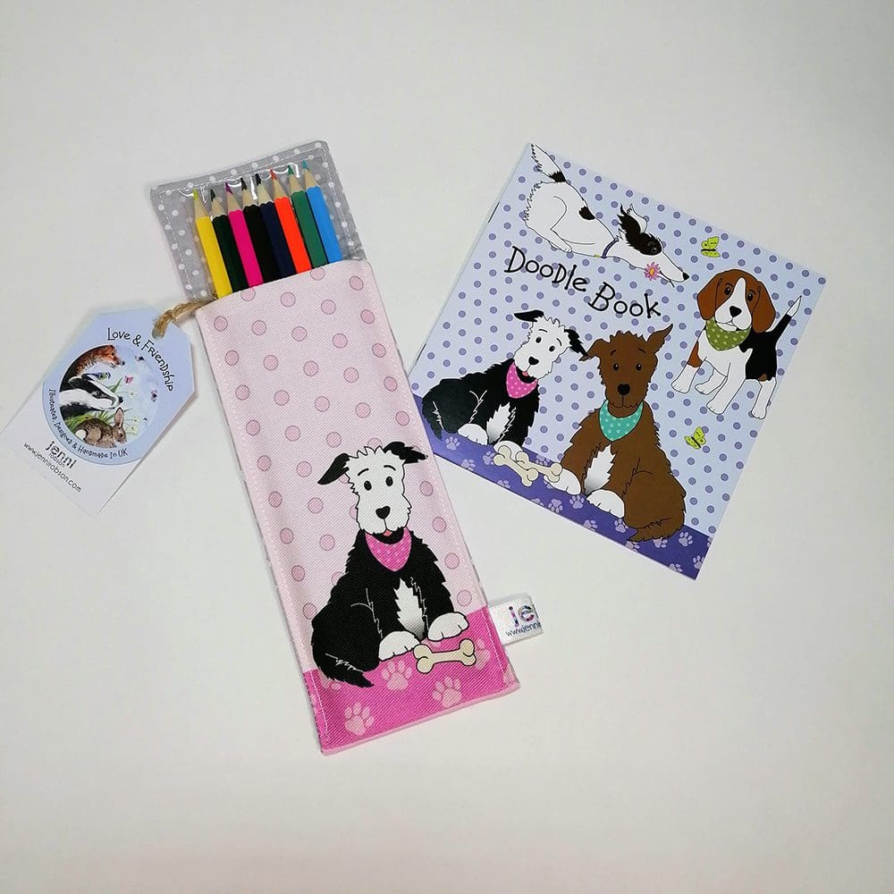 Kids Doodle Kit stationery set. Cotton pocket featuring a black and white dog containing 8 colouring pencils. Blue spotty square sketchbook featuring dogs