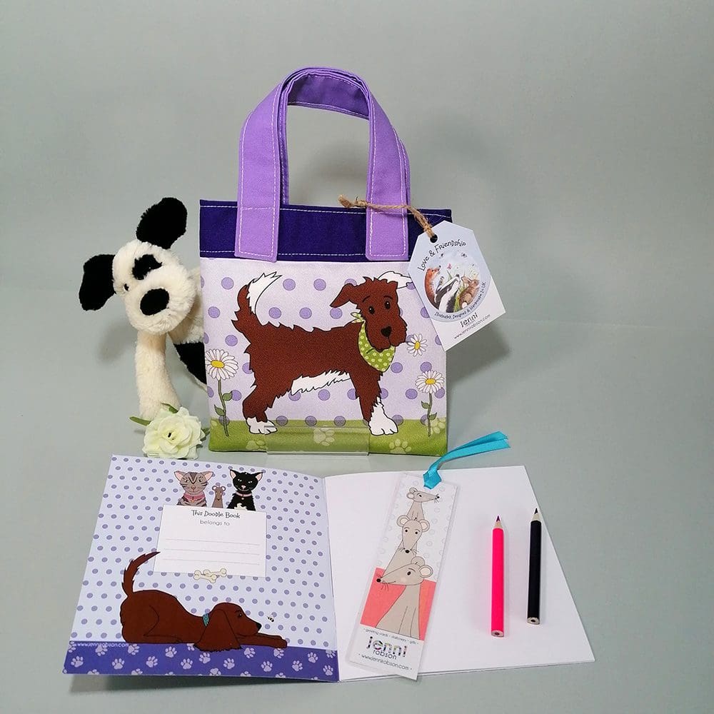 Gorgeous pale and dark purple cotton bookbag with water resistant lining featuring a smart brown dog in his best green bandana illustration. The bag contains a stapled blank 20 page sketchbook featuring a selection of dogs and furry friends, 14 mini colouring pencils with a laminated bookmark printed with a mouse theme.