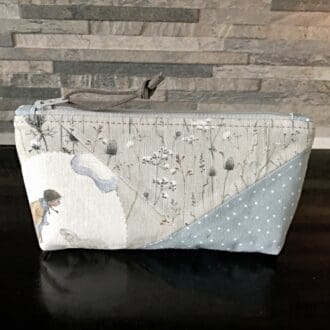 Small patchwork makeup bag on a reflective black surface. With winter themed patchwork focussing on a small girl with a large snowball
