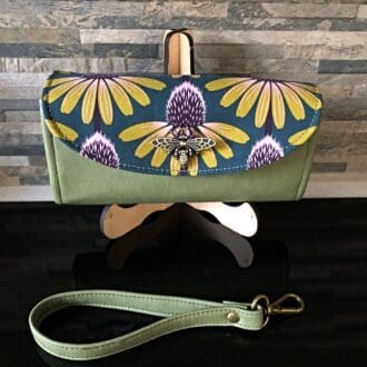 Ladies clutch wallet in olive faux leather featuring an echinacea print flap with large brass bumblebee clasp on a stand