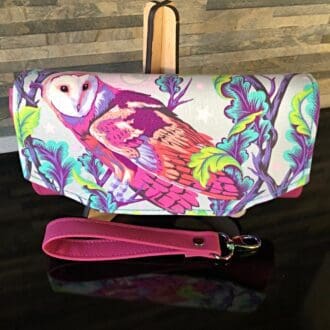 Ladies clutch wallet featuring Tula Pink Owl print flap with pink faux leather body on a stand