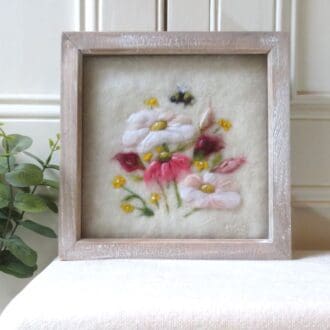 A handmade needle felted wool picture of a posy of flowers in a distressed natural wood box frame.
