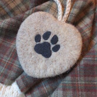 A handmade needle felted natural coloured wool heart hanging decoration featuring a dogs paw print in black.