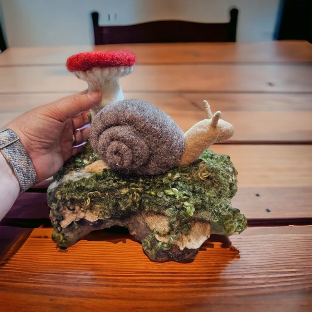 Hand holding a needle felted snail with toadstool