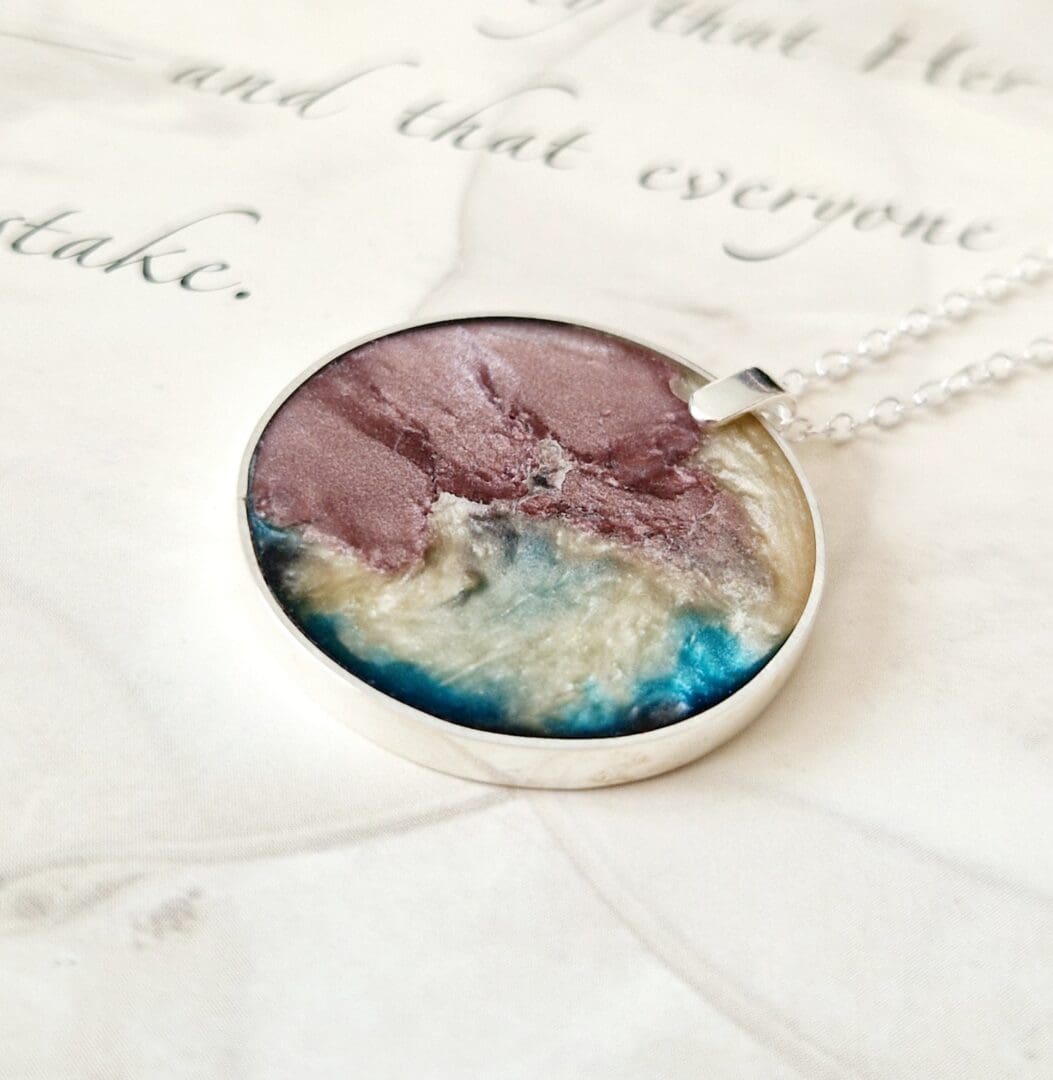 Sterling silver circular pendant filled with pale teracotta clay and gold and blue tones of pearlescent resin on a sterling silver trace chain