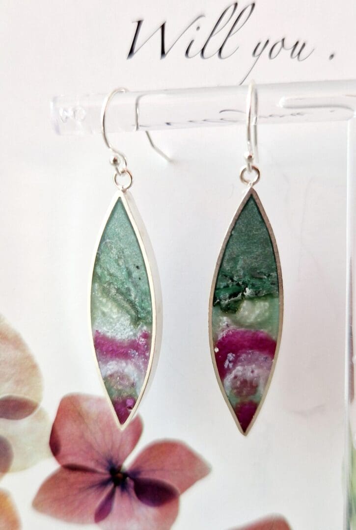 Sterling silver earrings with a leaf shape frame filled with sage green clay and rose pink tones of pearlescent resin on a sterling silver trace chain