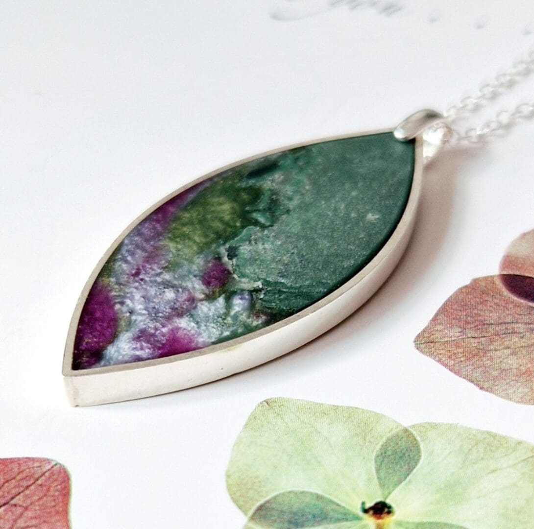 Sterling silver pendant with a leaf shape frame filled with sage green clay and rose pink tones of pearlescent resin on a sterling silver trace chain