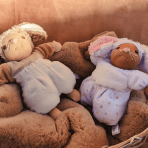 brown mouse doll with pale skin and white mouse doll with brown skin relaxing in a basket with a brown furry blanket, against a cinnamon background