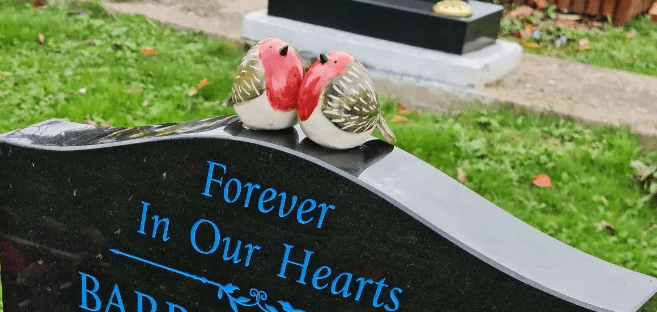 2 ceramic robins on top of a gravestone, the writing says "forever in our hearts"