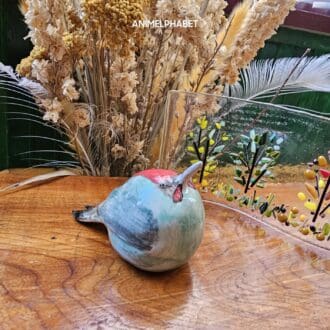 Ceramic green woodpecker on wood table with dried flowers and glass art in background