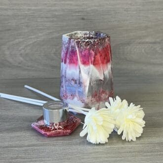 a reed diffuser made from epoxy resin in shades of pink white and silver. Has 3 reeds with floral heads for diffusing scent.