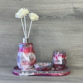 A resin reed diffuser, trinket dish, brush pot and tray in shades of pink and silver