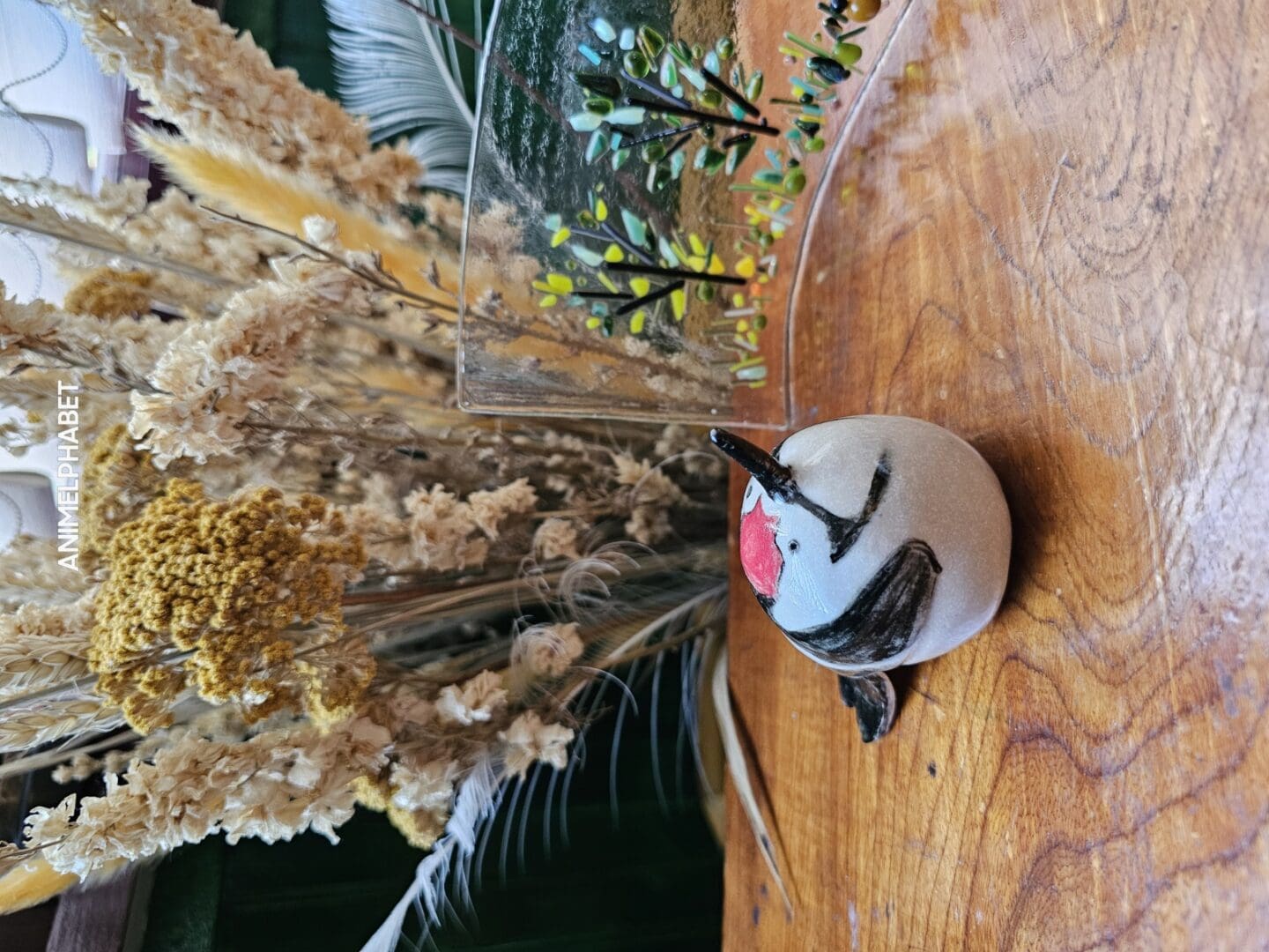 Ceramic lesser spotted woodpecker sat on a wooden table, with dried flowers behind and glass art to the side