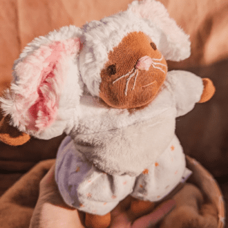 little white mouse doll with pink nose and brown skin balancing on a hand with a brown background