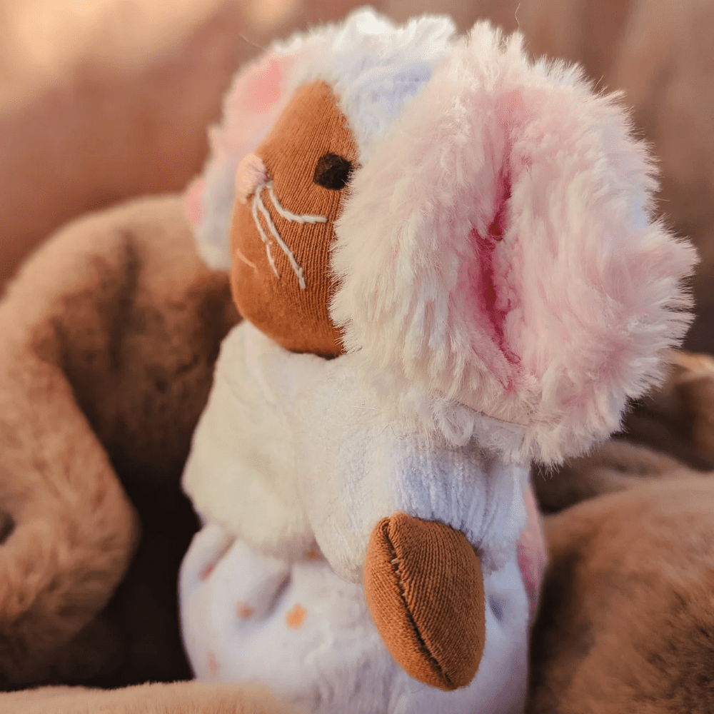 little mouse doll with brown skin and dark brown eyes looking outward in side profile with brown background.Hee fur is brilliant white and she has large floppy ears with pink fur inside.