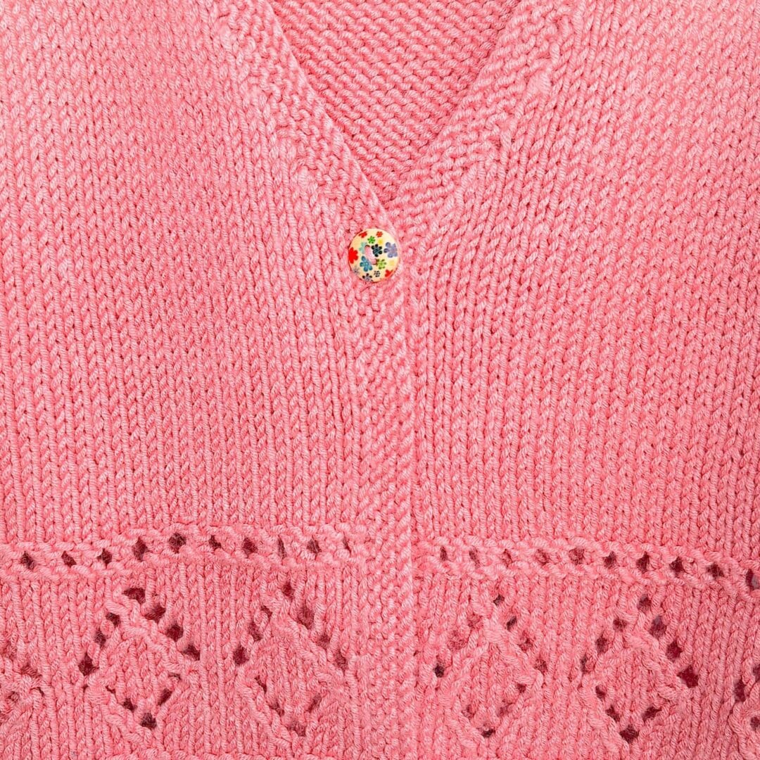 Detail of the diamond pattern and button fastening of an older childs cardigan. Hand knit from Ambel.