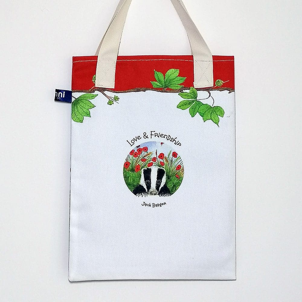 Back view of the badger and poppies bookbag showing a 'Love and Friendship' logo on reverse. Red trim on top with chestnut tree branch decoration and pale cream cotton handles