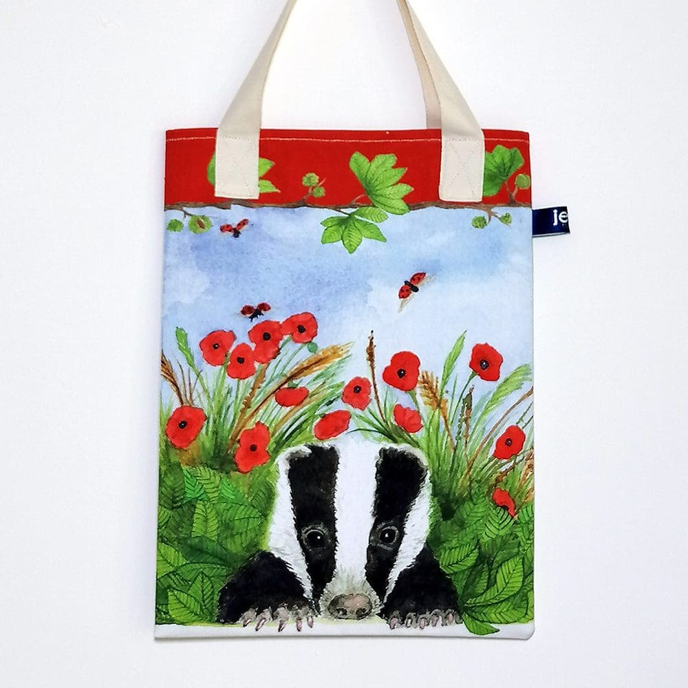 Wildlife bookbag featuring a badger cub amongst the red poppies and green leaves and grasses on the front. Red trim on top edge with chestnut tree branch decoration and pale cream cotton handles.