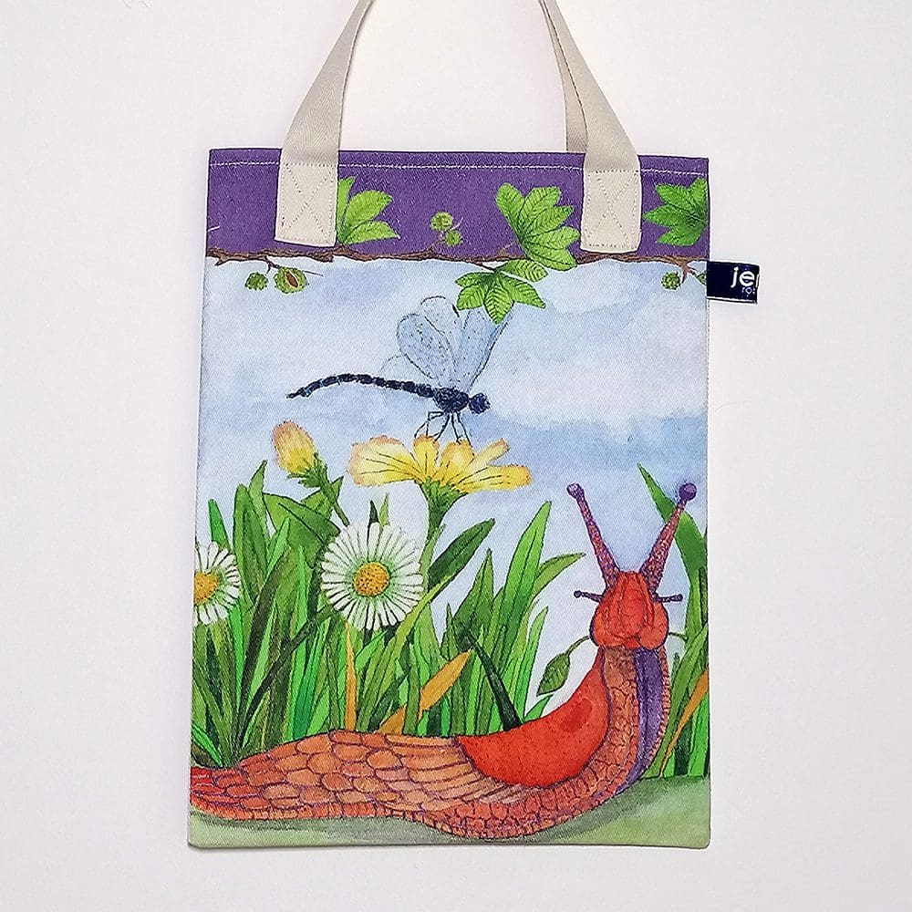 Wildlife bookbag featuring a dragonfly and slug amongst the grass and daisies on the front. Purple trim on top edge with chestnut tree branch decoration and pale cream cotton handles.