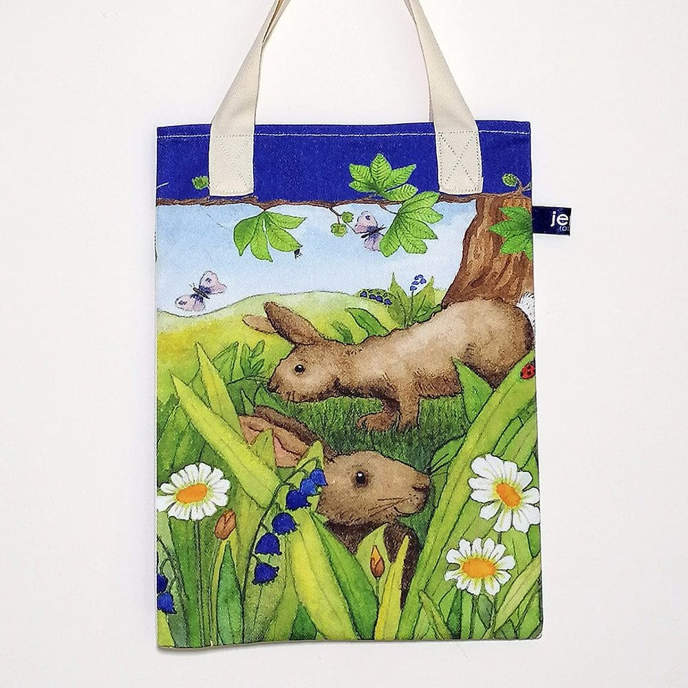 Wildlife bookbag featuring two brown rabbits hiding amongst the grass and daisies on the front. Blue trim on top edge with chestnut tree branch decoration and pale cream cotton handles.