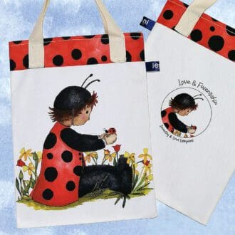 Ladybug bookbag, on the front featuring toddler Dorothy in a bright red spotty ladybug costume sat amongst the flowers chatting to Spot the ladybug. On reverse is the 'Love and Friendship logo with a little close up of Dorothy and Spot. Spotty ladybug design trim on top edge and pale cream cotton handles.