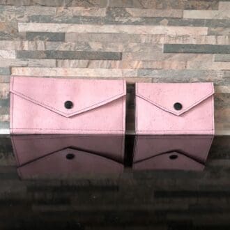 A pair of slim ladies slim wallets in pink cork with black snaps on a brick background