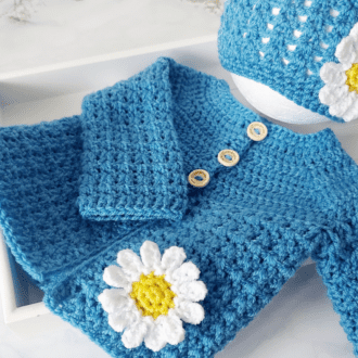 Crochet Cardigan and hat gift set available in sizes newborn up to 24 months, the set is crochet with a 'v' stitch pattern adding texture, and both items are finished off with a daisy that has a yellow centre and white petals