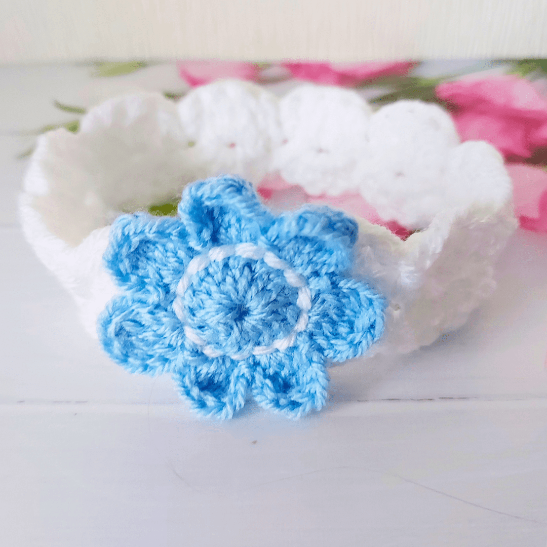 A white crochet alice band with a pale blue flower attached to the front