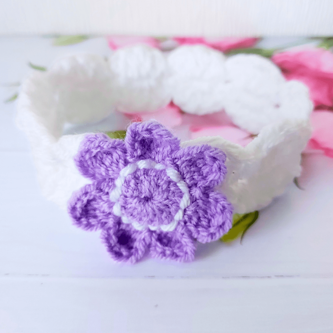 A white crochet headband with a purple flower attached to the front