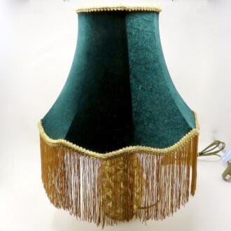 A handmade scalloped lampshade in dark green velvet and with a gold fringe.