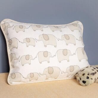 A small cushion featuring elephants with a childs stuffed toy in the foreground.