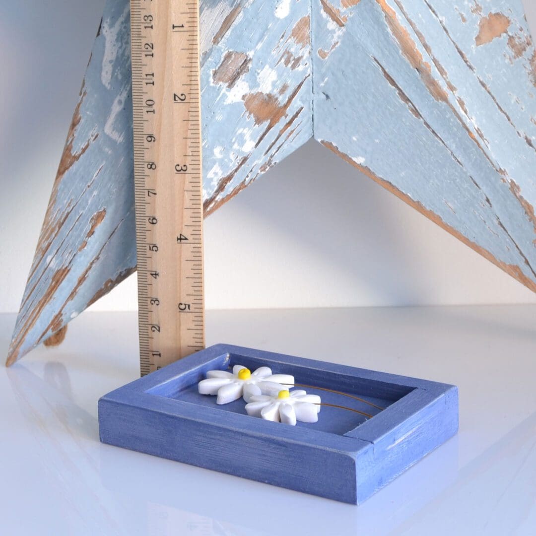 Dark blue wooden frame with two clay daisies on wire inside