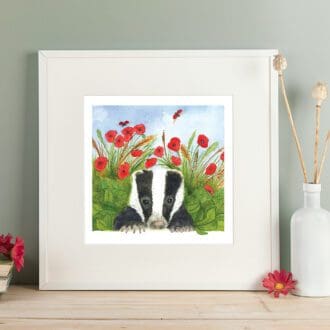 Wildlife art print of a badger cub hiding amongst the leaves and red poppies. Giclee print with a white mount. Shown in a readily available standard size square white frame