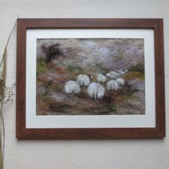 A handmade needle felted wool picture of Swaledale sheep on a winter fell in a dark wood effect frame.