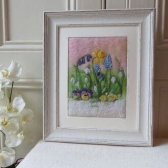 A handmade needle felted wool picture of spring flowers in a white shabby chic wood effect frame.