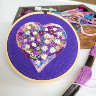 Hand embroidered flowers filling a heart shape, purple colours on purple fabric 4 inch size hoop.