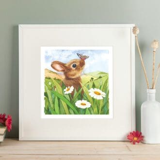 Wildlife art print of a brown rabbit sat amongst white daisies and green grasses with a butterfly on his nose. Giclee print with a white mount. Shown in a readily available standard size square white frame