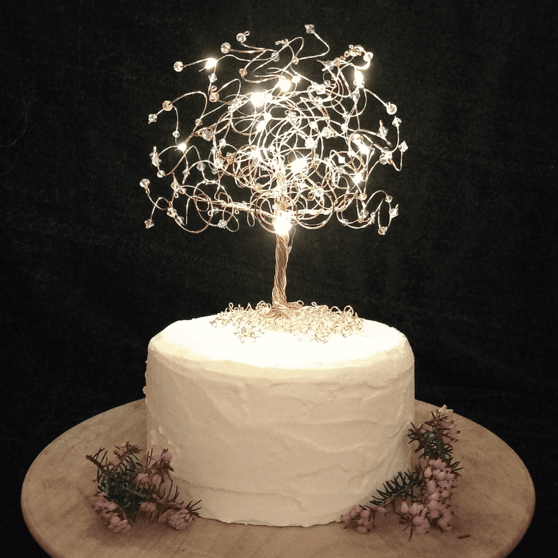 Rose Gold wire cake topper tree decorated with micro-lights and sitting on a white cake tier.