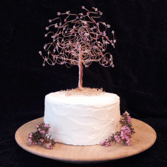 Rose Gold wire tree decorated with a pink mix of crystals and sitting on a white cake tier, decorated with two sprigs of purple heather,