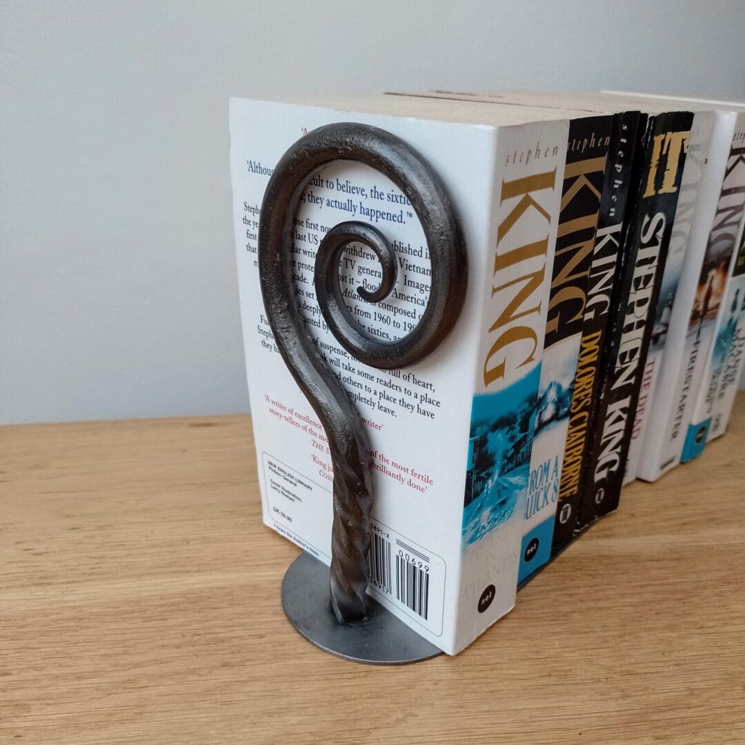 A pair of hand forged metal bookends with a spiral end and a large plate for the books to sit on.