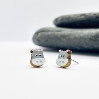 hand painted hippopotamus earrings on a white background next to grey pebbles