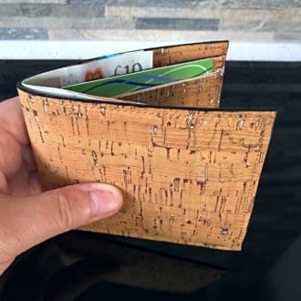 Traditional bi-fold wallet in natural cork with silver flecks effect held to show proportion against a brick backdrop.