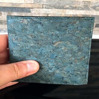 Traditional cork wallet in deep sea green held to show proportion against a brick backdrop.
