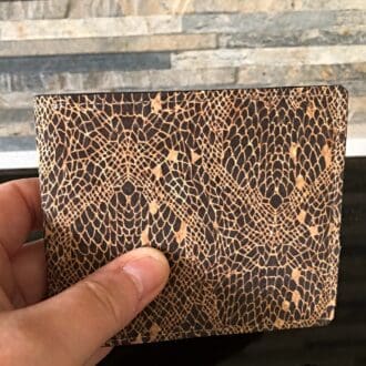 Traditional cork wallet in black snakeskin effect held to show proportion against a brick backdrop.
