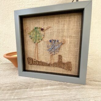 Grey square framed wire art of two birds on a branch.